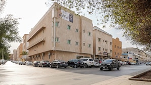 Un edificio de varios pisos con fachada color crema, varios balcones y una fila de coches estacionados a lo largo de la calle.