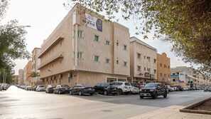 Un immeuble à plusieurs étages, doté d’une façade beige, de plusieurs balcons et d’une rangée de voitures garées le long de la rue.