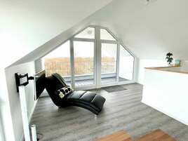 A spacious room with a large window, a black leather chair, and a wooden shelf.