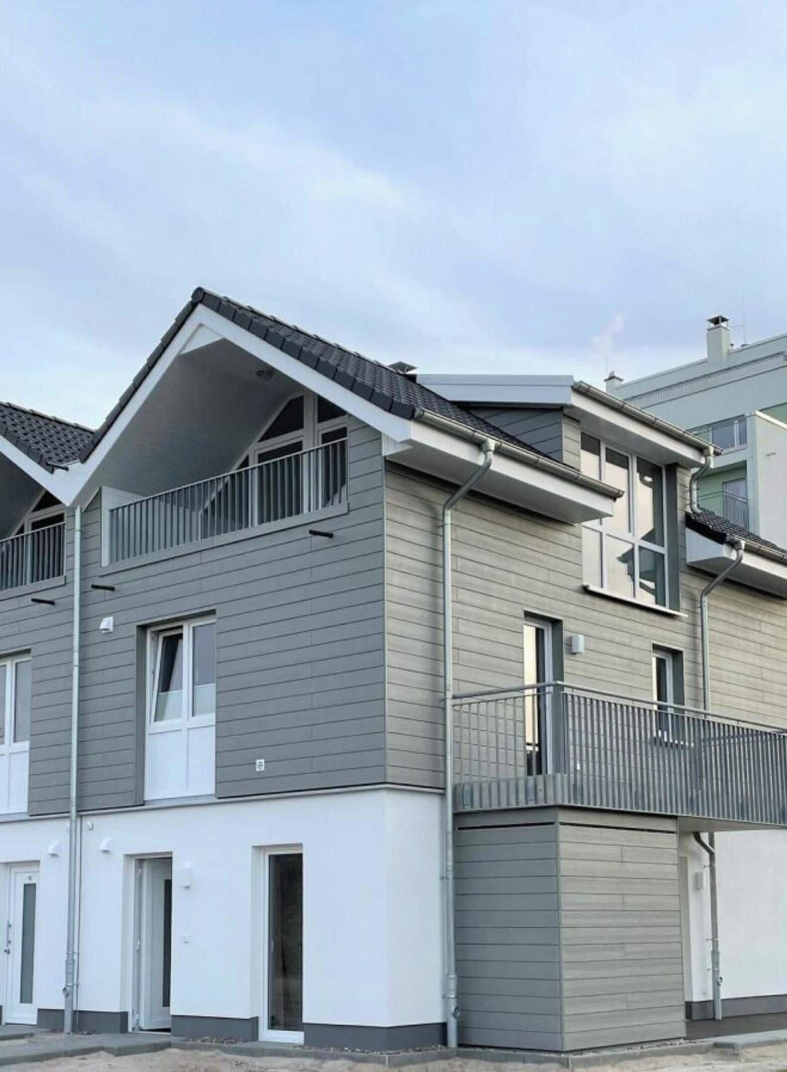 A modern two-story residential building with a grey exterior, a balcony on the upper floor, and a visible garage door.