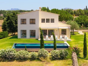 Ein modernes, zweistöckiges Haus mit Swimmingpool, umgeben von Grünflächen und Bäumen.