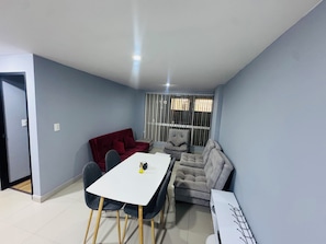 A compact living space with a dining table, two sofas, and a window with blinds.