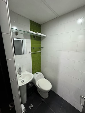 A bathroom with a white sink, a toilet, and a glass shelf with a towel.
