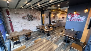 Interior de una cafetería con paredes de ladrillo, mesas de madera y luces colgantes.