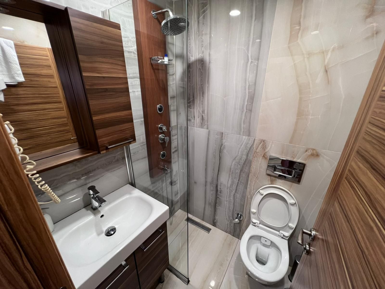 Ein modernes Badezimmer mit einer Marmerdusche, einem weißen Waschbecken und einer Toilette.