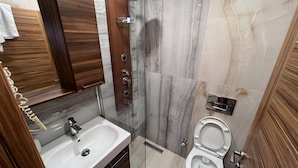 Un baño moderno con ducha de mármol, lavamanos blanco y un inodoro.