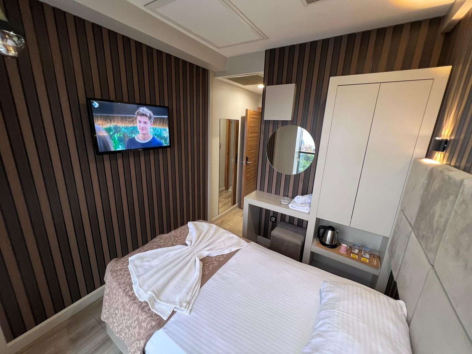 A hotel room with a bed, a television mounted on the wall, a mirror, and a wardrobe.