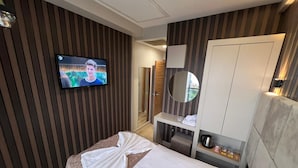 Una habitación de hotel con una cama, un televisor montado en la pared, un espejo y un armario.