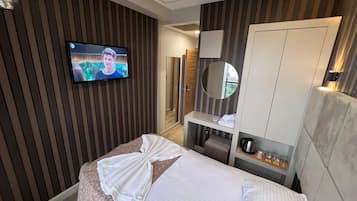 A hotel room with a bed, a television mounted on the wall, a mirror, and a wardrobe.