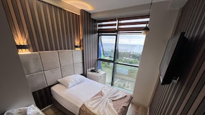 Un dormitorio moderno con una cama grande, una mesita de noche, un televisor y una ventana con vistas al exterior.