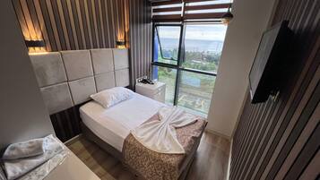 Ein modernes Schlafzimmer mit einem großen Bett, einem Nachttisch, einem kleinen Tisch daneben, einem Fernseher und einem Fenster mit Blick nach außen.