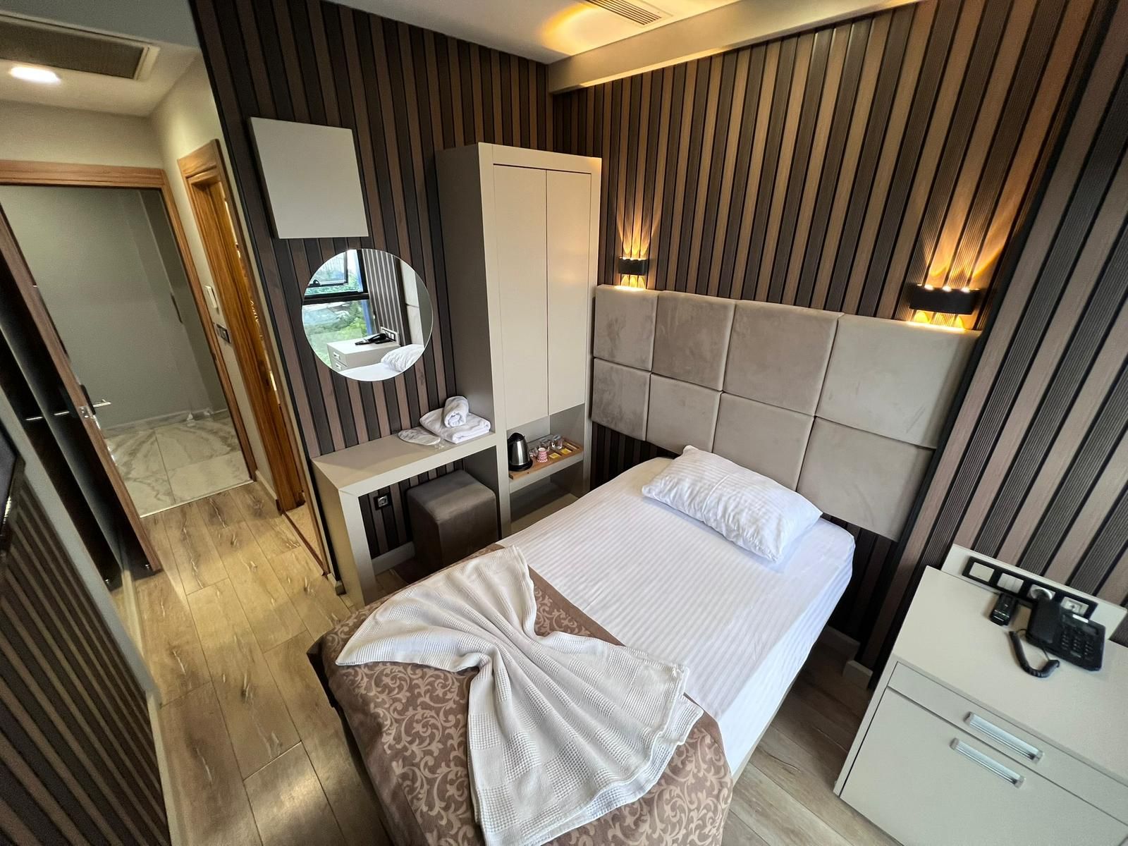 Ein Hotelzimmer mit Bett, Nachttisch, Spiegel, Kleiderschrank und Schreibtisch mit Telefon.