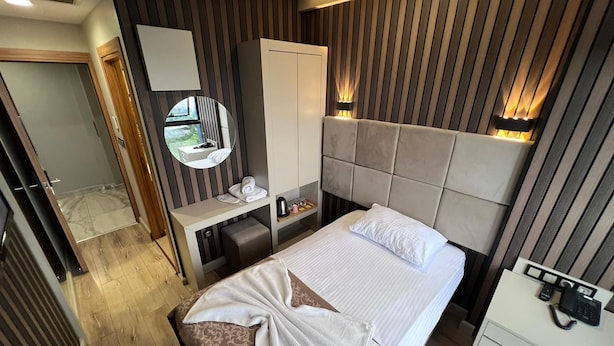 Una habitación de hotel con cama, mesita de noche, espejo, armario y escritorio con teléfono.