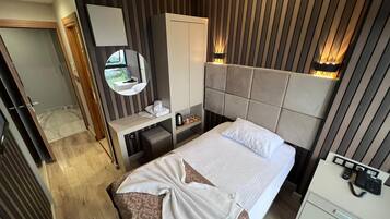 Ein Hotelzimmer mit Bett, Nachttisch, Spiegel, Kleiderschrank und Schreibtisch mit Telefon.