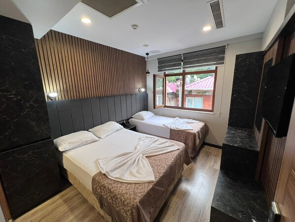 A hotel room with two beds, a wooden headboard, a window with a view, and a flat-screen TV.