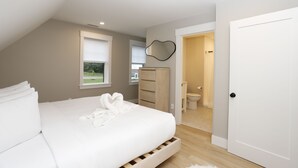 Quarto com cama, cômoda, espelho e porta para um banheiro.
