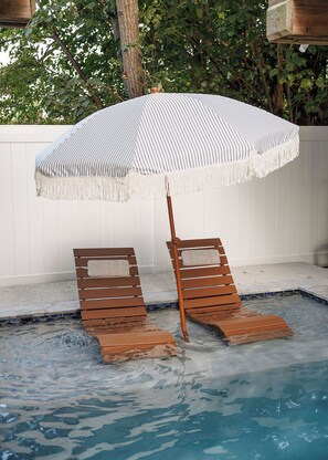 A poolside area with two wooden lounge chairs and a striped umbrella. - Coastal Luxury Meets Resort Living in East End Historic District Galveston (Galveston)