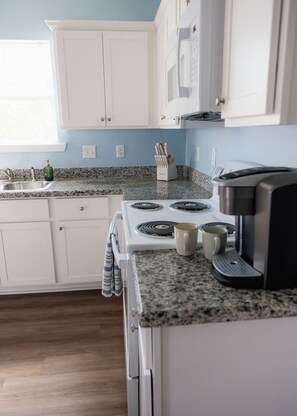 A kitchen with white cabinets, a granite countertop, a stove, and a coffee maker. - Coastal Luxury Meets Resort Living in East End Historic District Galveston (Galveston)