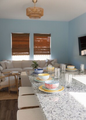 A kitchen with a granite countertop, a dining table set with bowls and glasses, a sofa, and a ceiling light fixture. - Coastal Luxury Meets Resort Living in East End Historic District Galveston (Galveston)