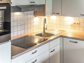 A modern kitchen with a stainless steel sink, a built-in oven, and white cabinetry. - Gästehaus Steger incl. Sommercard by Interhome (Zell am See)