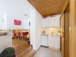 A compact kitchen with white cabinets, a wooden ceiling, and a dining area with wooden chairs and a table. - Gästehaus Steger incl. Sommercard by Interhome (Zell am See)