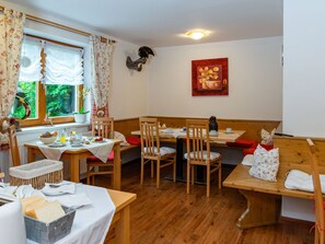 Un coin repas accueillant avec des tables et des chaises en bois, une fenêtre avec des rideaux et un tableau accroché au mur.
