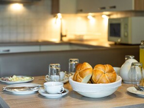A breakfast setting with a bowl of bread, cups, and a teapot on a wooden table. - Gästehaus Steger incl. Sommercard by Interhome (Zell am See)