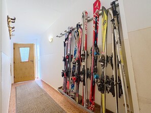 Un couloir où une rangée de paires de skis est fixée au mur, et une porte se trouve au fond.