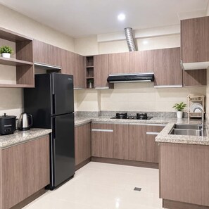 A modern kitchen with wooden cabinets, a black refrigerator, a gas stove, and a sink. - Cozy Stay for Couple (Parañaque)