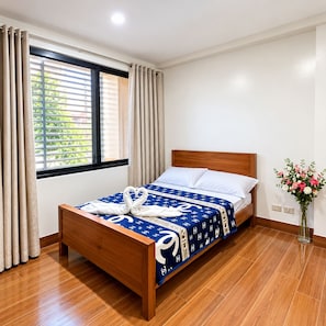 A hotel room with a wooden bed, a window with blinds, and a vase of flowers. - Cozy Stay for Couple (Parañaque)