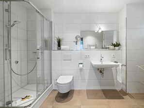 Ein modernes Badezimmer mit Duschkabine aus Glas, einer weißen Toilette, einem Waschbecken mit Spiegel darüber und einer Topfpflanze auf der Ablagefläche.