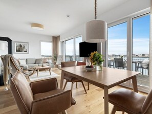Ein modernes Wohnzimmer mit einem großen Esstisch, Ledersesseln, einer Couch und einem an der Wand montierten Fernseher.