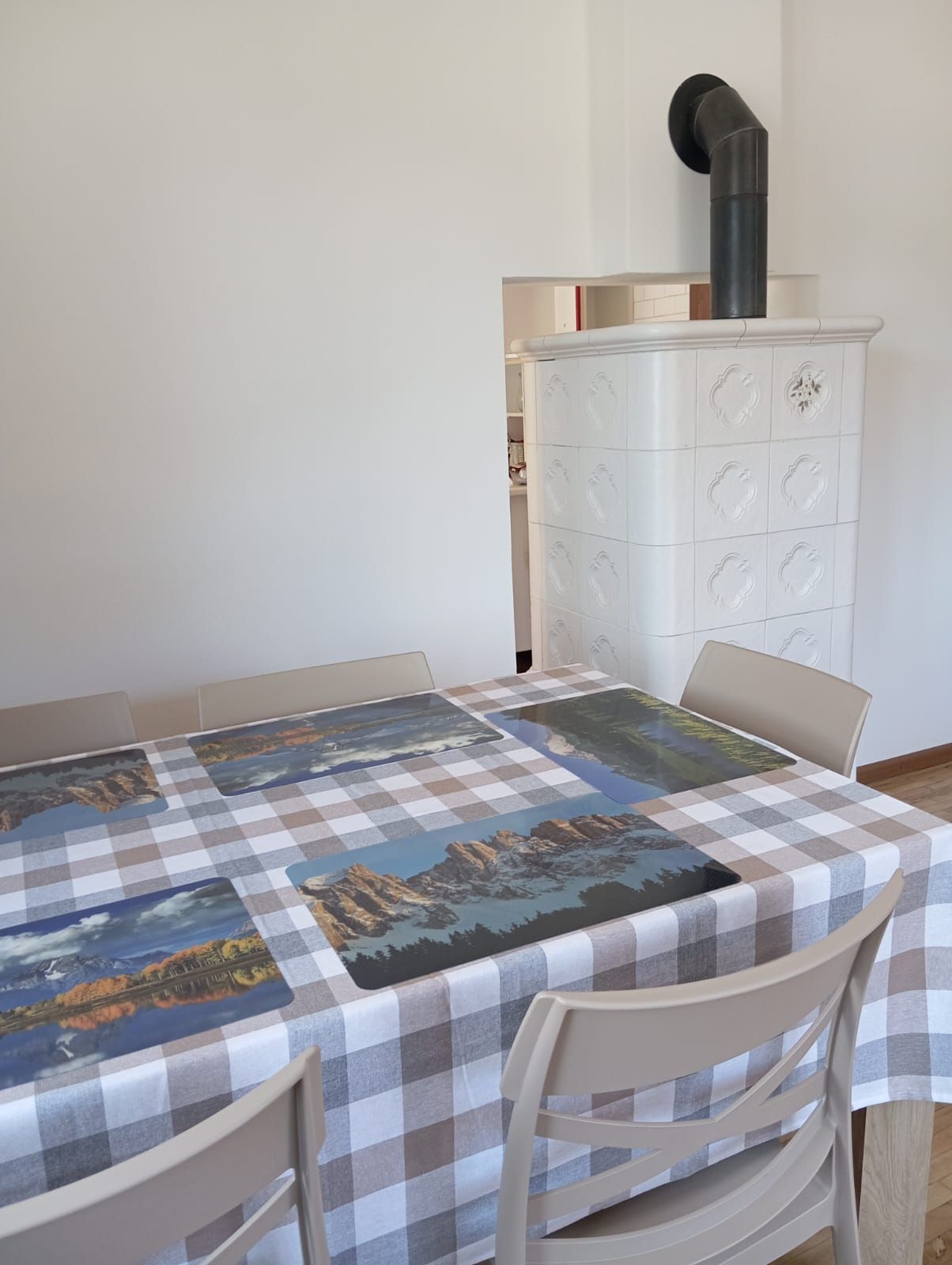 A dining area with a checkered tablecloth, white chairs, and a white cabinet with decorative patterns.