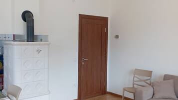 Una stanza con pavimento in legno, una porta marrone, un armadietto bianco con un oggetto nero sopra, un divano beige e un tavolo a scacchi con una sedia.