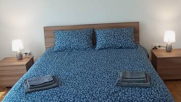 A bed with a floral patterned bedspread, two pillows, two bedside tables with lamps, and a wooden floor.