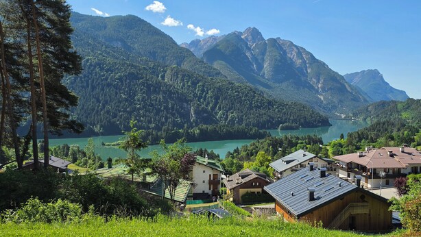 Paesaggio montuoso con un lago, circondato da zone boschive e edifici residenziali.