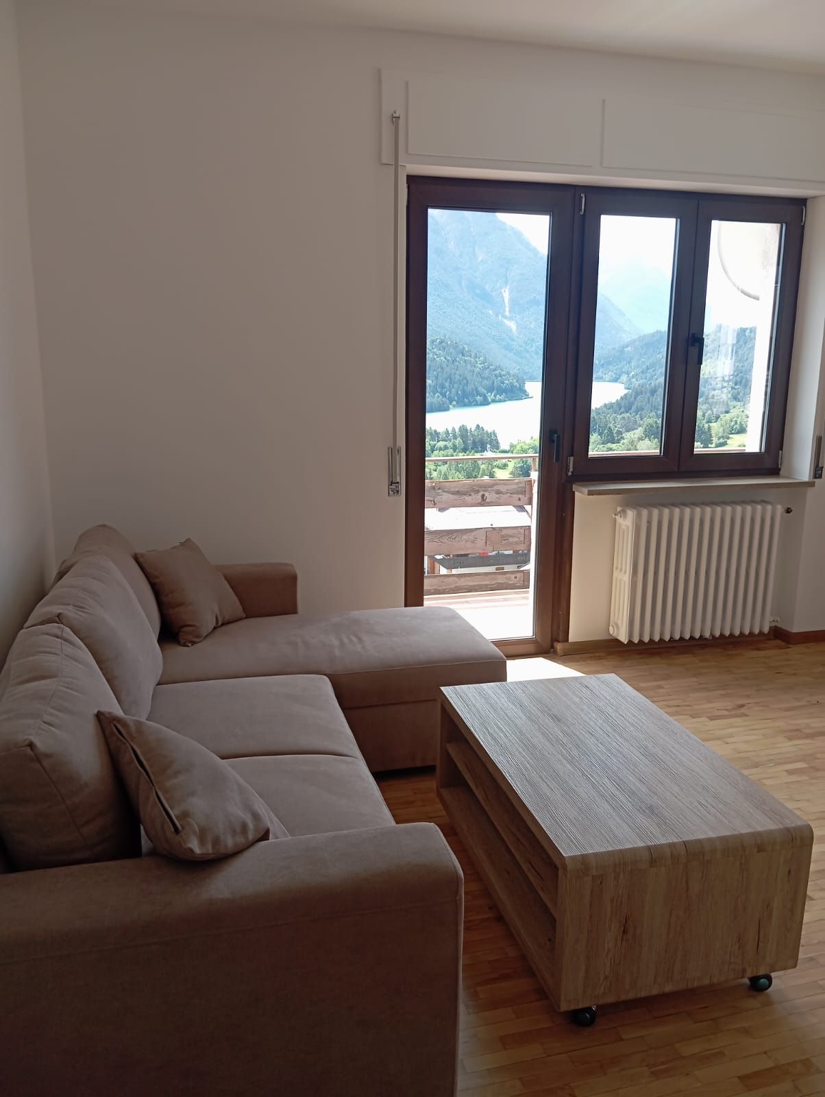 Una sala de estar con un sofá modular, una mesa de centro de madera y un ventanal con vistas a un paisaje montañoso.