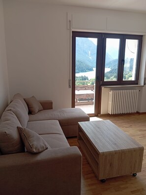 Sala de estar com sofá seccional, mesa de centro de madeira e uma grande janela com vista para uma paisagem montanhosa.