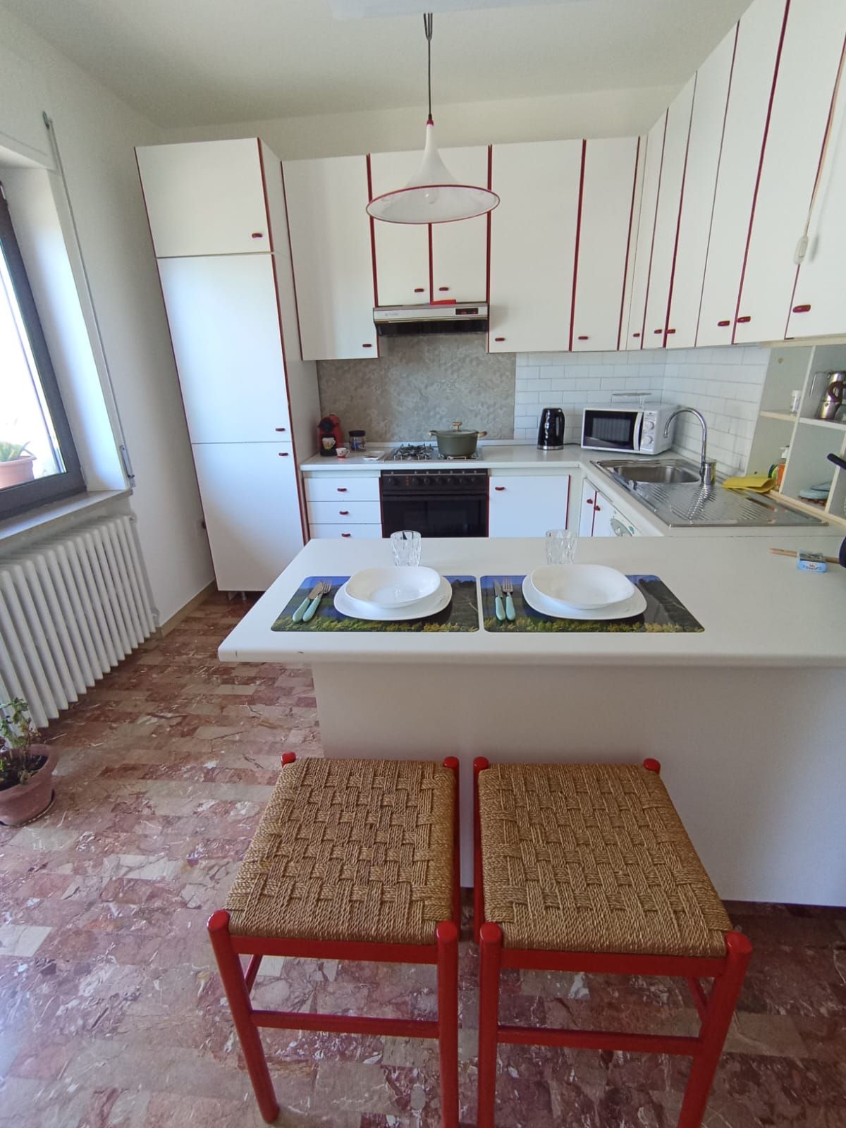 A kitchen with white cabinets, a central island with two stools, a gas stove, a microwave, and a sink.