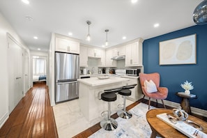 A modern kitchen with white cabinetry, stainless steel appliances, and a central island with bar stools. - Modern Queen West Escape Sleeps 6 with Parking (Toronto)