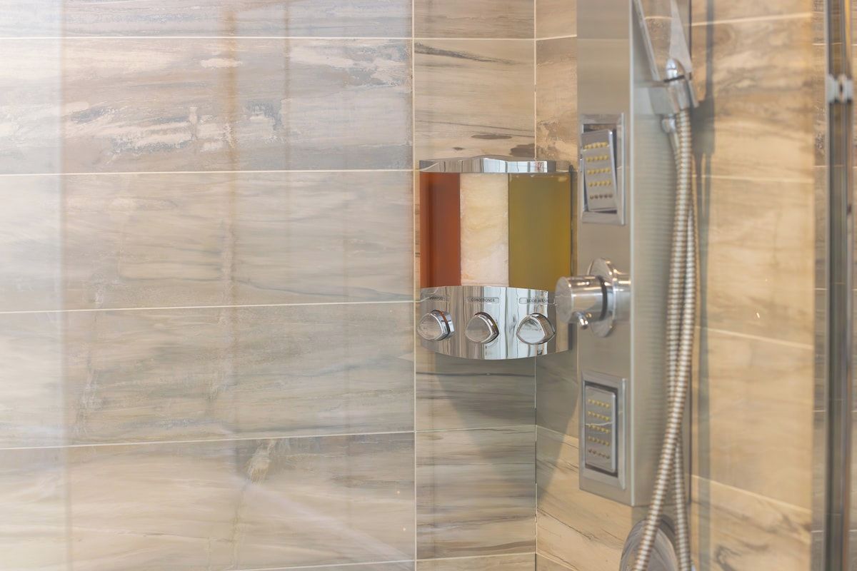 A bathroom with a shower enclosure, a control panel, and a tiled wall.