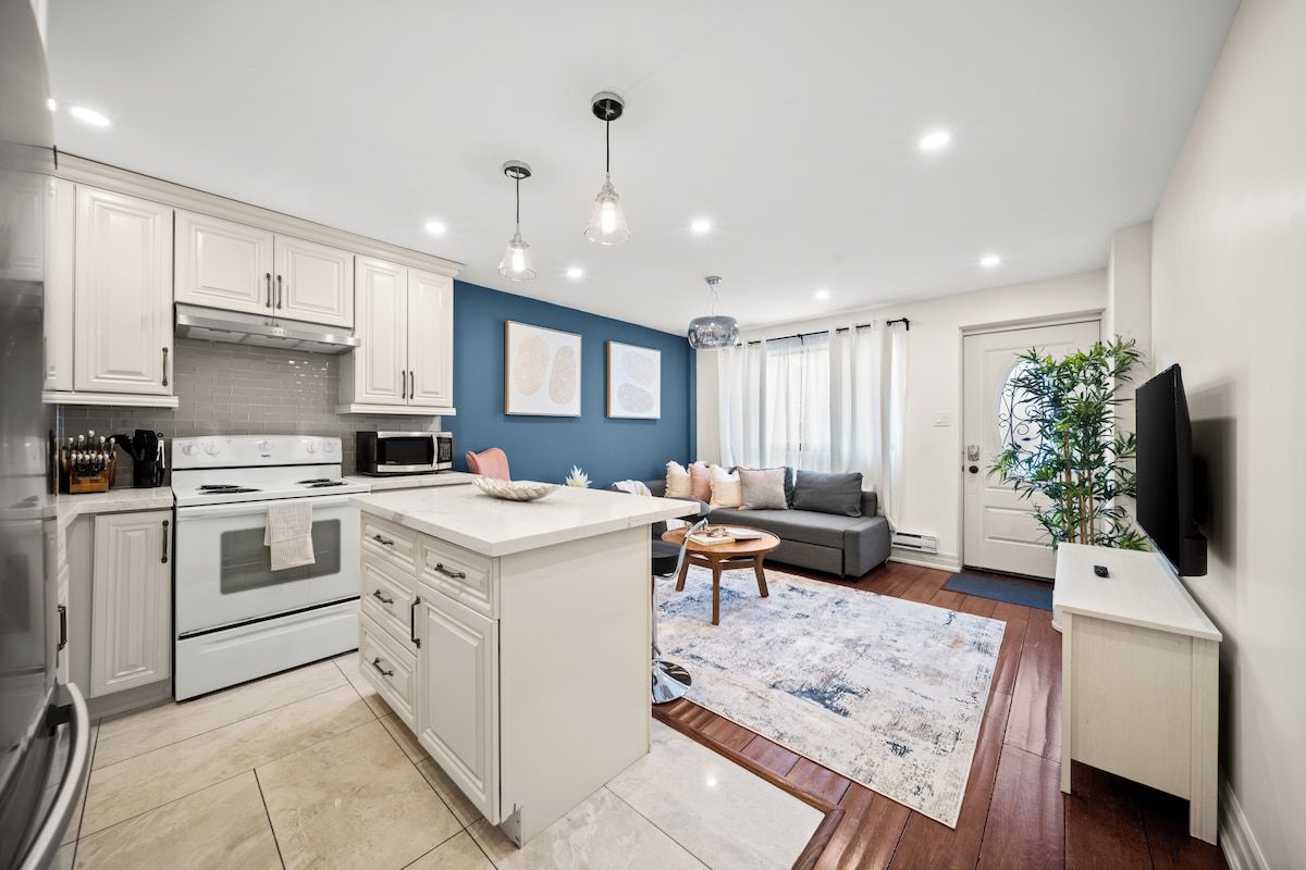 A modern kitchen with white cabinets, a central island, and a dining area with a sofa and coffee table.