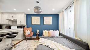 Un dormitorio moderno con una cama, un escritorio y una silla. Hay una zona de cocina con armarios y electrodomésticos.