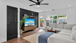 A modern living room with a flat-screen TV, a ceiling fan, and a view of the outdoors through large windows. - **SUNSET ON FOGARTY @ MIDTOWN** Newly Renovated Home & Pool + Last Key White Glo (Key West)