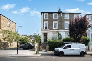 A residential street with a two-story house, parked cars, and a tree. - Between Camden & Kings Cross. Above the Ordinary - Pass the Keys (London)