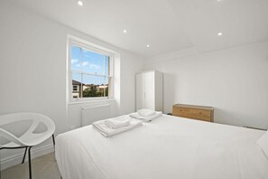 A modern bedroom with a large bed, a wardrobe, a chair, and a window with a view of houses. - Between Camden & Kings Cross. Above the Ordinary - Pass the Keys (London)