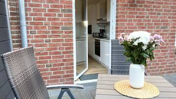 Un patio al aire libre con una silla de mimbre, una mesa con un mantel tejido y un jarrón de flores.