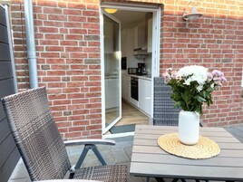 Un patio al aire libre con una silla de mimbre, una mesa con un mantel tejido y un jarrón de flores.