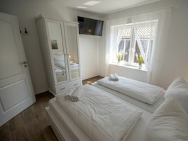 Un dormitorio con cama, armario, televisor montado en la pared y ventana con cortinas.