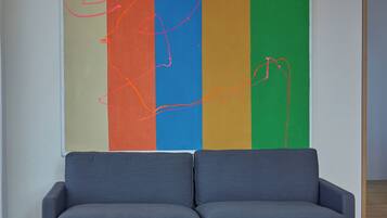 A modern living room with a grey sofa, a coffee table with books and a glass, and a colorful abstract painting on the wall.